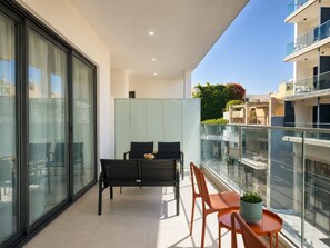 A balcony with a glass railing, a table, two chairs, and a potted plant. - City Center Apartment Ermou Street (Larnaca)