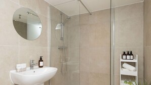 Ein modernes Badezimmer mit Duschkabine aus Glas, einem weißen Waschbecken und einem Spiegel.