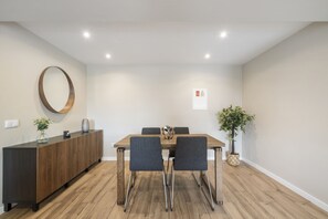 A modern dining area with a wooden table, two chairs, a round mirror, and a potted plant. - Oceanea Apartment by Homie (Santa Cruz)