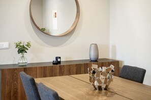 A modern dining area with a wooden table, grey chairs, a decorative vase, and a round mirror on the wall.