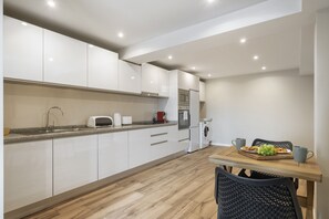 A modern kitchen with white cabinets, a granite countertop, and a dining area with a wooden table and chairs.