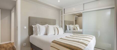 A modern bedroom with a large bed, a mirror, and a sliding door.