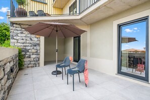 A patio with two chairs, a table, and a large umbrella. - Oceanea Apartment by Homie (Santa Cruz)