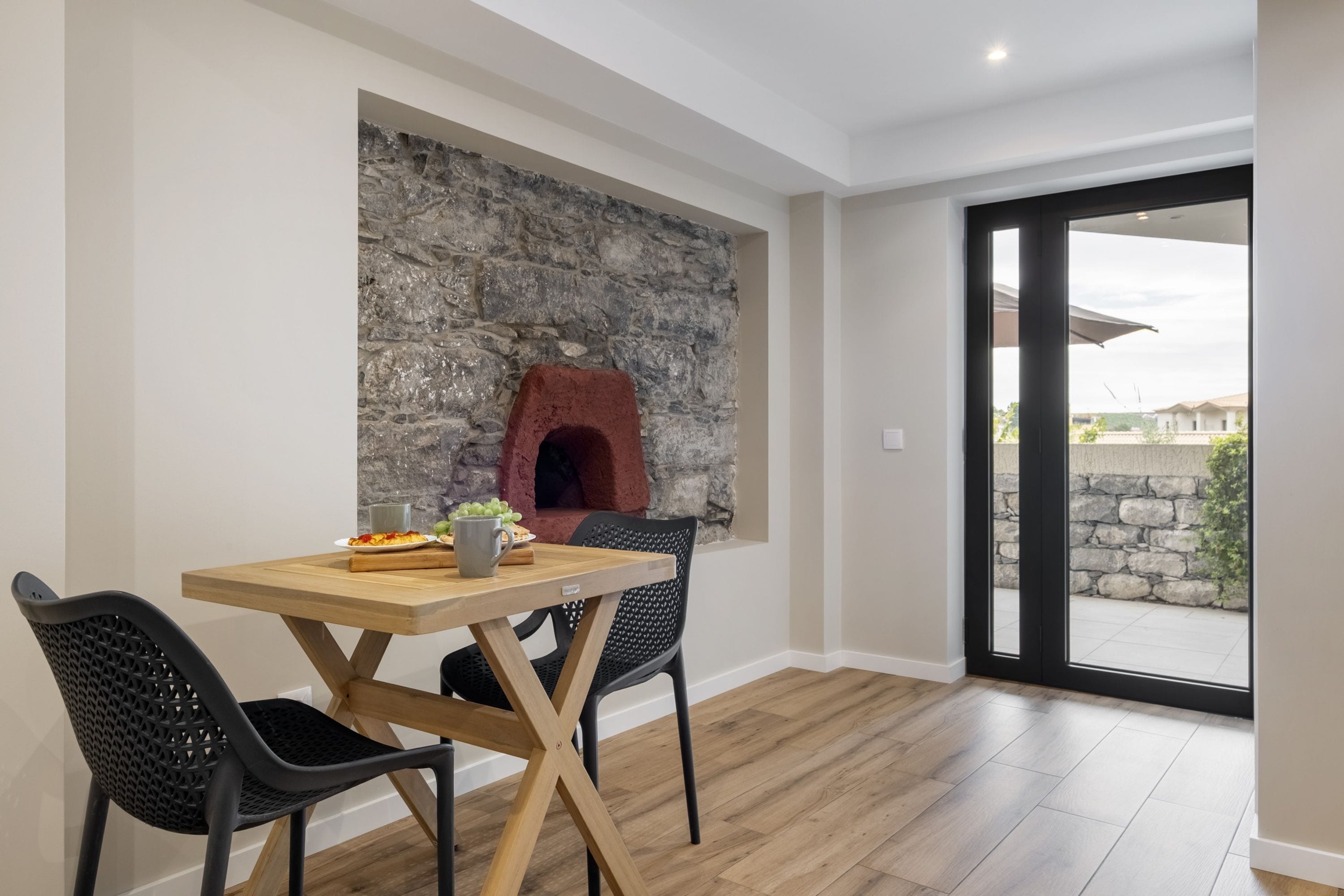A dining area with a stone wall, a pizza oven, and a view through a glass door.