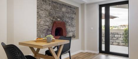 Uma área de refeições com parede de pedra, forno a pizza e vista através de uma porta de vidro.