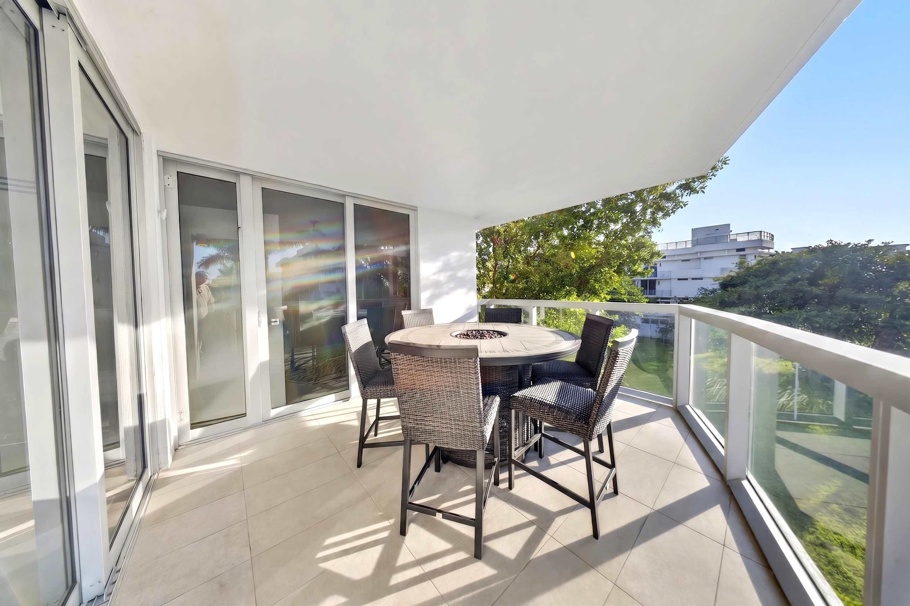 A balcony with a round table and chairs, a fire pit, and a view of greenery and buildings.