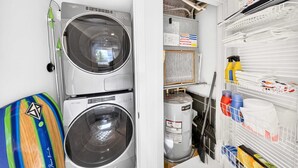 A laundry room with two stacked washers and dryers, a water heater, and shelves with cleaning supplies. - Chic Bay Harbor 3BR Rooftop Pool Free Parking (Bay Harbor Islands)