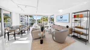 A modern living room with a glass dining table, sofas, a coffee table, and a bookshelf. - Chic Bay Harbor 3BR Rooftop Pool Free Parking (Bay Harbor Islands)