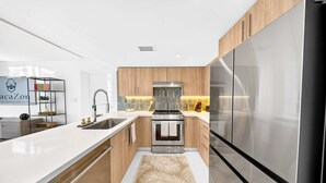 A modern kitchen with a stainless steel refrigerator, wooden cabinets, and a white countertop. - Chic Bay Harbor 3BR Rooftop Pool Free Parking (Bay Harbor Islands)