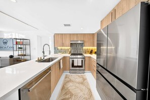 A modern kitchen with a stainless steel refrigerator, wooden cabinets, and a white countertop. - Chic Bay Harbor 3BR Rooftop Pool Free Parking (Bay Harbor Islands)