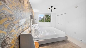 A bedroom with a bed, a window, a wall with a leaf pattern, and a hanging light fixture. - Chic Bay Harbor 3BR Rooftop Pool Free Parking (Bay Harbor Islands)