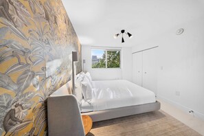 A bedroom with a bed, a window, a wall with a leaf pattern, and a hanging light fixture. - Chic Bay Harbor 3BR Rooftop Pool Free Parking (Bay Harbor Islands)