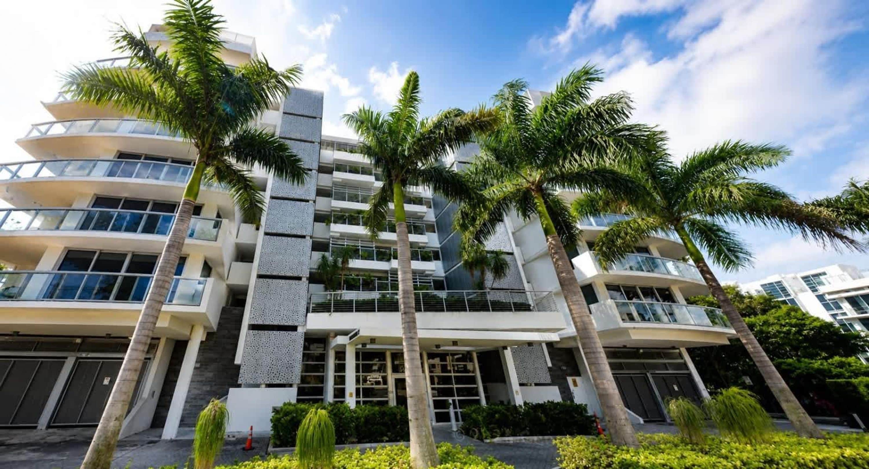 A multi-story hotel with balconies, palm trees, and a clear sky.