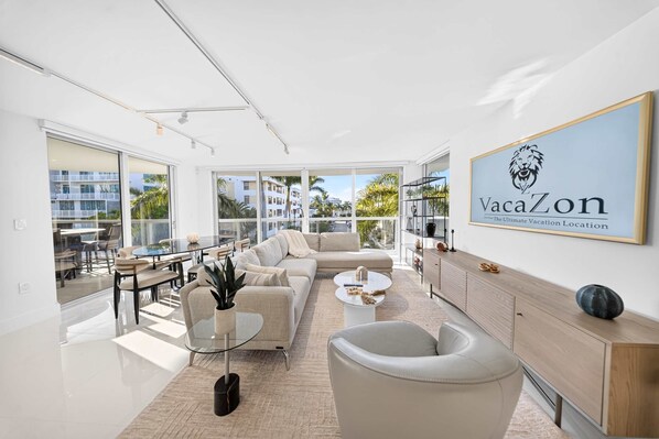 A modern living room with a sofa, coffee table, and a dining area with chairs and a glass table. - Chic Bay Harbor 3BR Rooftop Pool Free Parking (Bay Harbor Islands)
