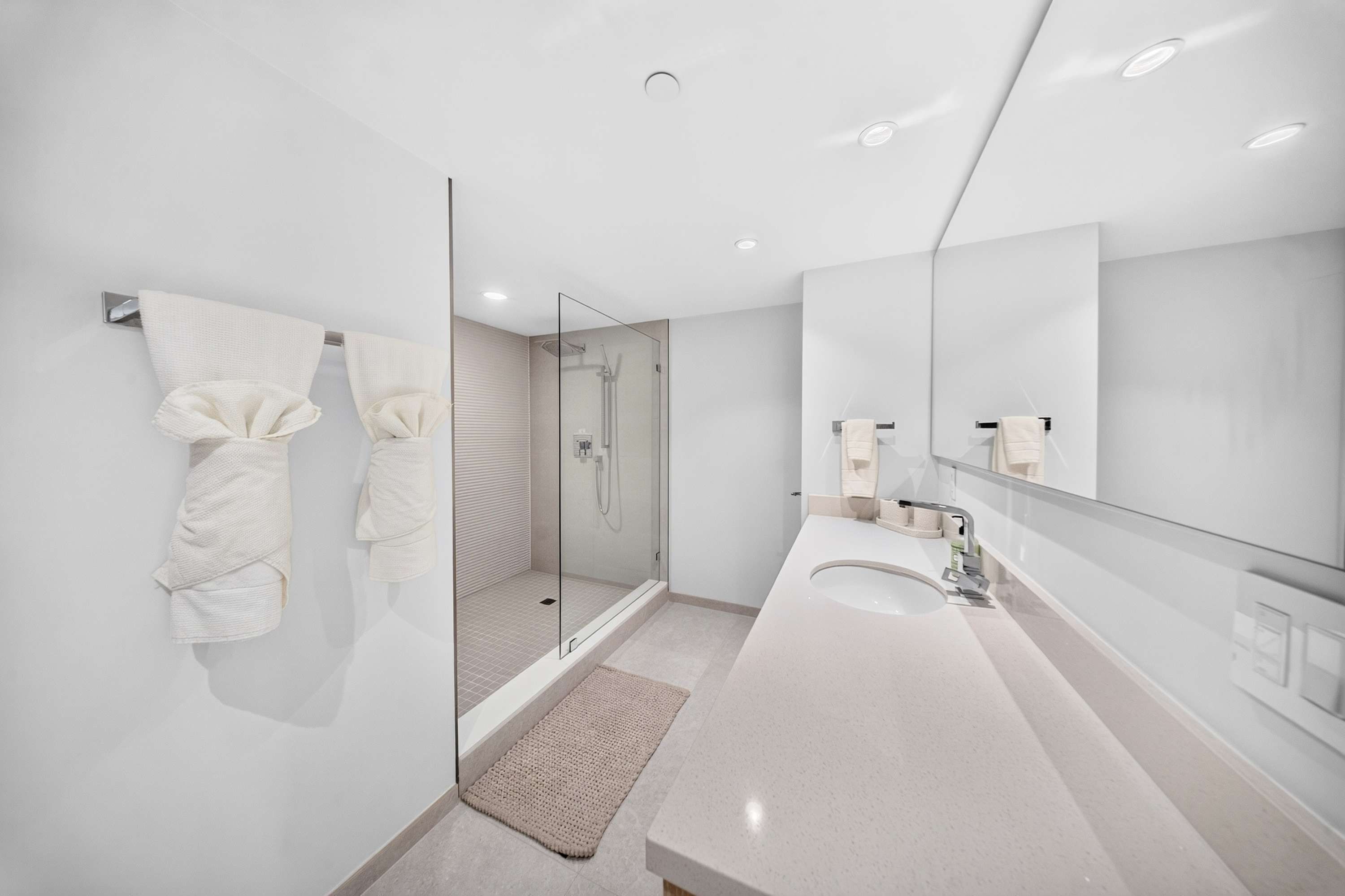 Un baño moderno con ducha envuelta en vidrio, un espejo grande y un lavabo blanco.