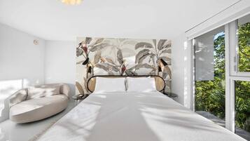 Quarto moderno com uma cama grande, um sofá e vista para o verde pela janela.