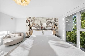 Quarto moderno com uma cama grande, um sofá e vista para o verde pela janela.