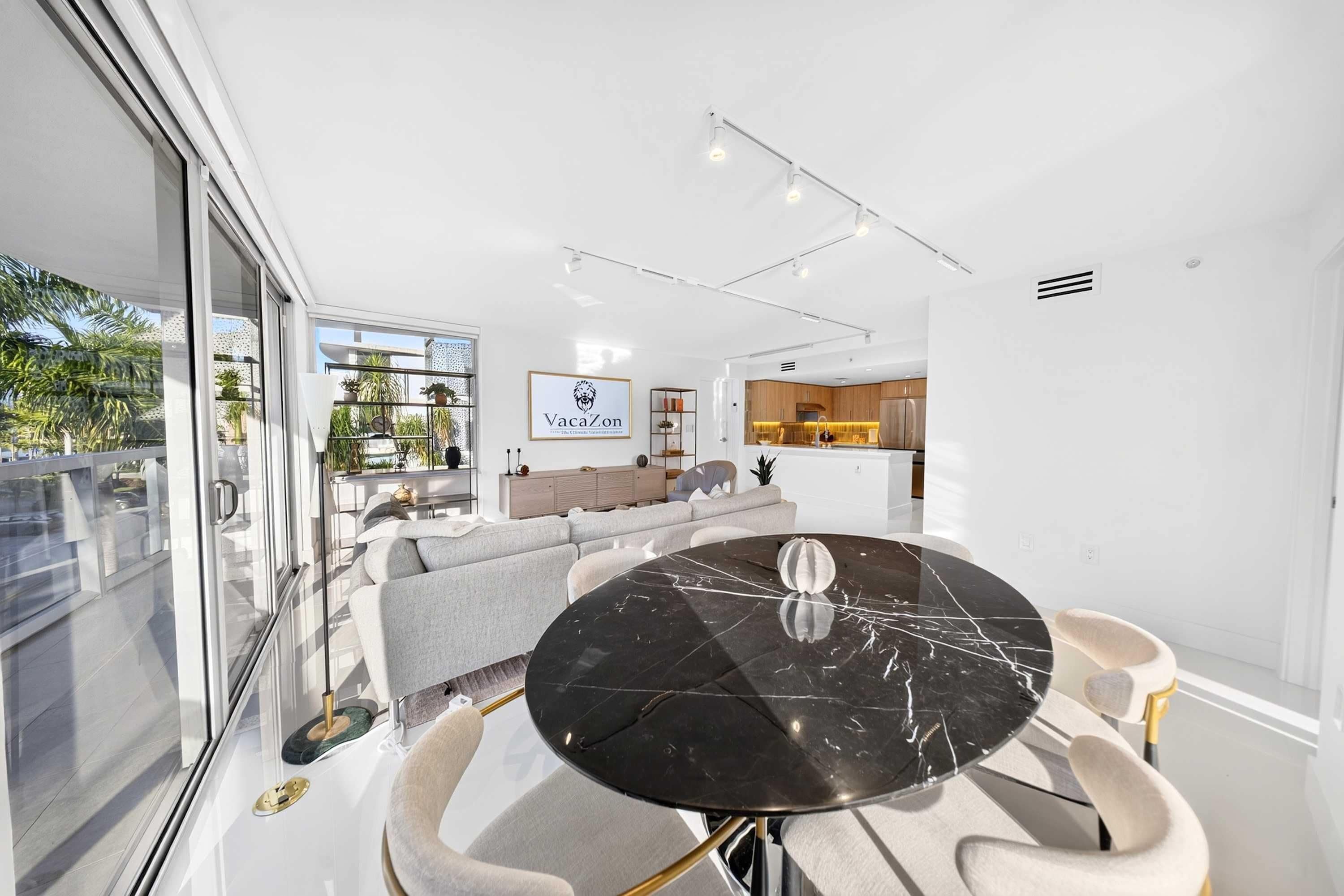 Interior moderno com área de jantar destacando uma mesa de mármore preto, um conjunto de sofás e uma cozinha ao fundo.