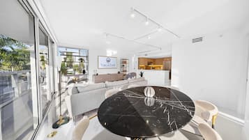 Interior moderno com área de jantar destacando uma mesa de mármore preto, um conjunto de sofás e uma cozinha ao fundo.