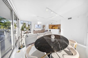 Interior moderno com área de jantar destacando uma mesa de mármore preto, um conjunto de sofás e uma cozinha ao fundo.