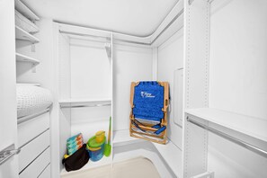 Um armário branco com prateleiras, cabideiro e um pequeno espaço de armazenamento com produtos de limpeza.