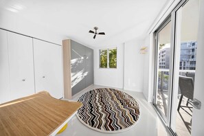 A modern room with a ceiling fan, a large window, and a patterned rug. - Chic Bay Harbor 3BR Rooftop Pool Free Parking (Bay Harbor Islands)