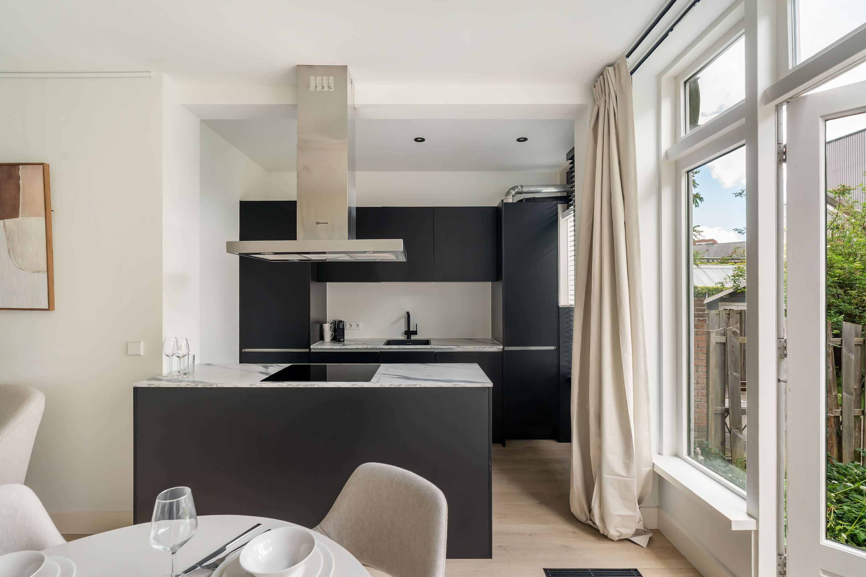 A modern kitchen with a central island, a dining area with a table and chairs, and a large window with curtains.