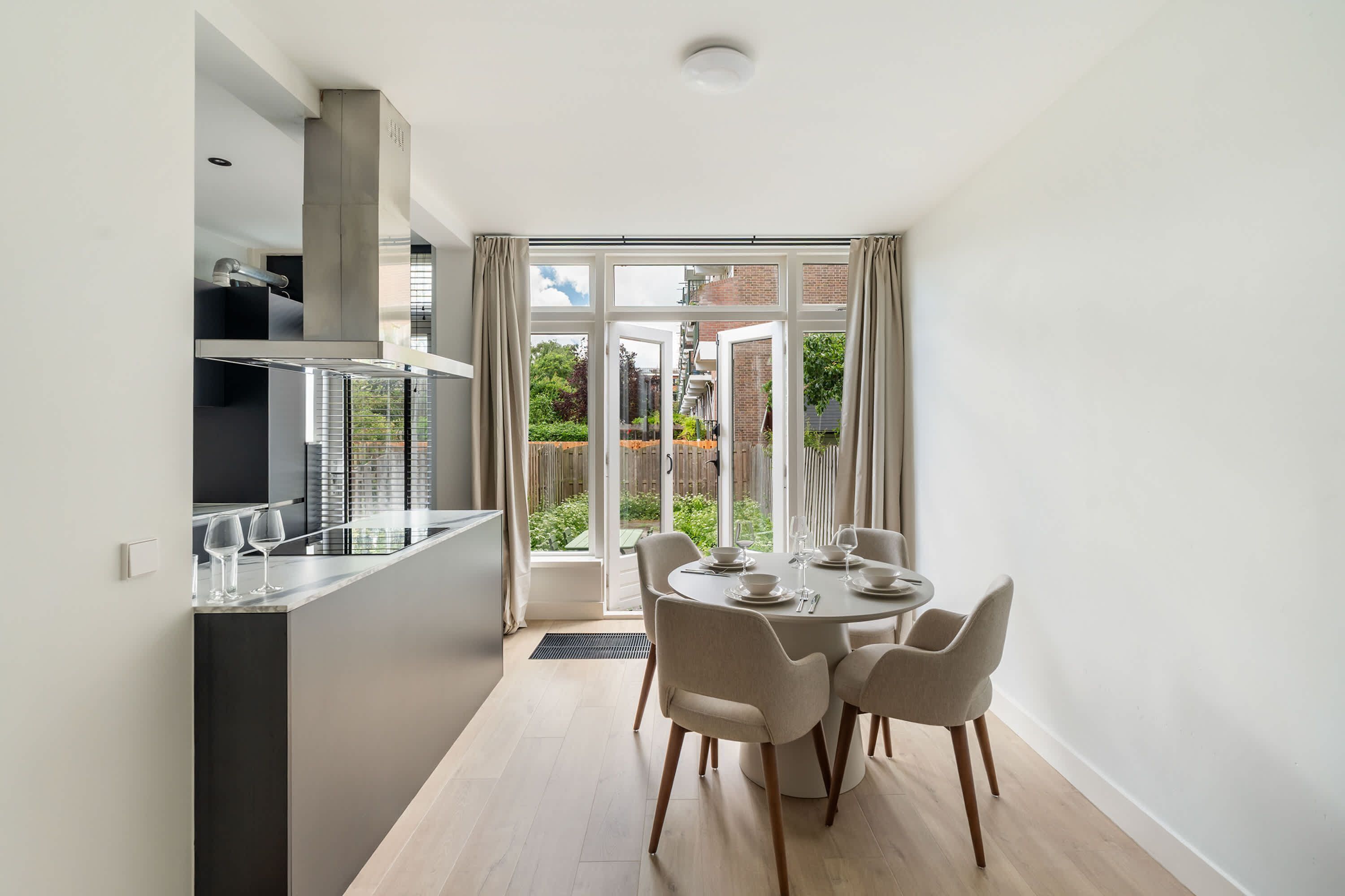 A modern kitchen with a dining area, large windows, and a view of the outside.