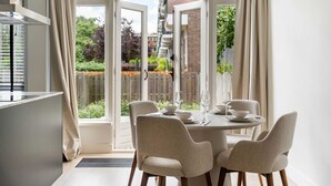 A dining area with a table set for four, chairs, and a view of a garden through large windows. - Urban Oasis With Garden in Rotterdam (Rotterdam)