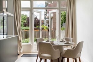 Ein Essbereich mit einem Tisch für vier Personen, Stühlen und Blick auf einen Garten durch große Fenster.