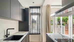 A modern kitchen with a black countertop, a sink, and a window with blinds. - Urban Oasis With Garden in Rotterdam (Rotterdam)