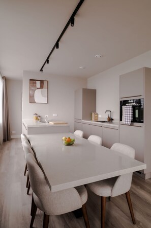 A modern kitchen with a central island, white cabinetry, and a dining area with a white table and chairs. - 2BR Rooftop Terrace in Rotterdam City Centre (Rotterdam)