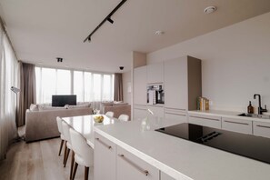 Uma cozinha moderna com uma ilha central, uma área de jantar com sofá e cadeiras, e uma bancada com pia e livros.