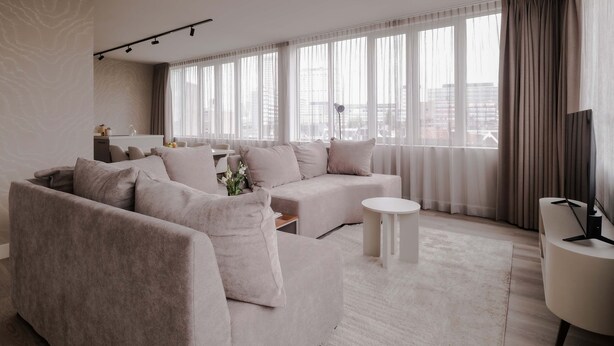 A modern living room with a sectional sofa, a round coffee table, and a large window with sheer curtains. - City Center Penthouse w Free Parking City Views (Rotterdam)