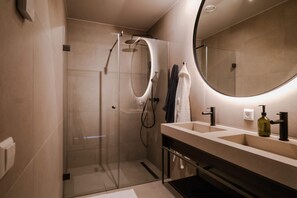 Casa de banho moderna com cabine de duche em vidro, um espelho grande e toucador com lavatório e porta-toalhas.