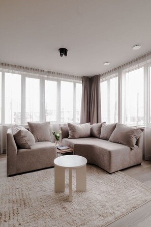 A modern living room with a sectional sofa, a round coffee table, and large windows with sheer curtains. - 2BR Penthouse Rotterdam City Centre (Rotterdam)