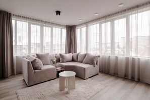 A modern living room with a sofa set, a coffee table, and a view of the city through large windows. - 2BR Penthouse Rotterdam City Centre (Rotterdam)
