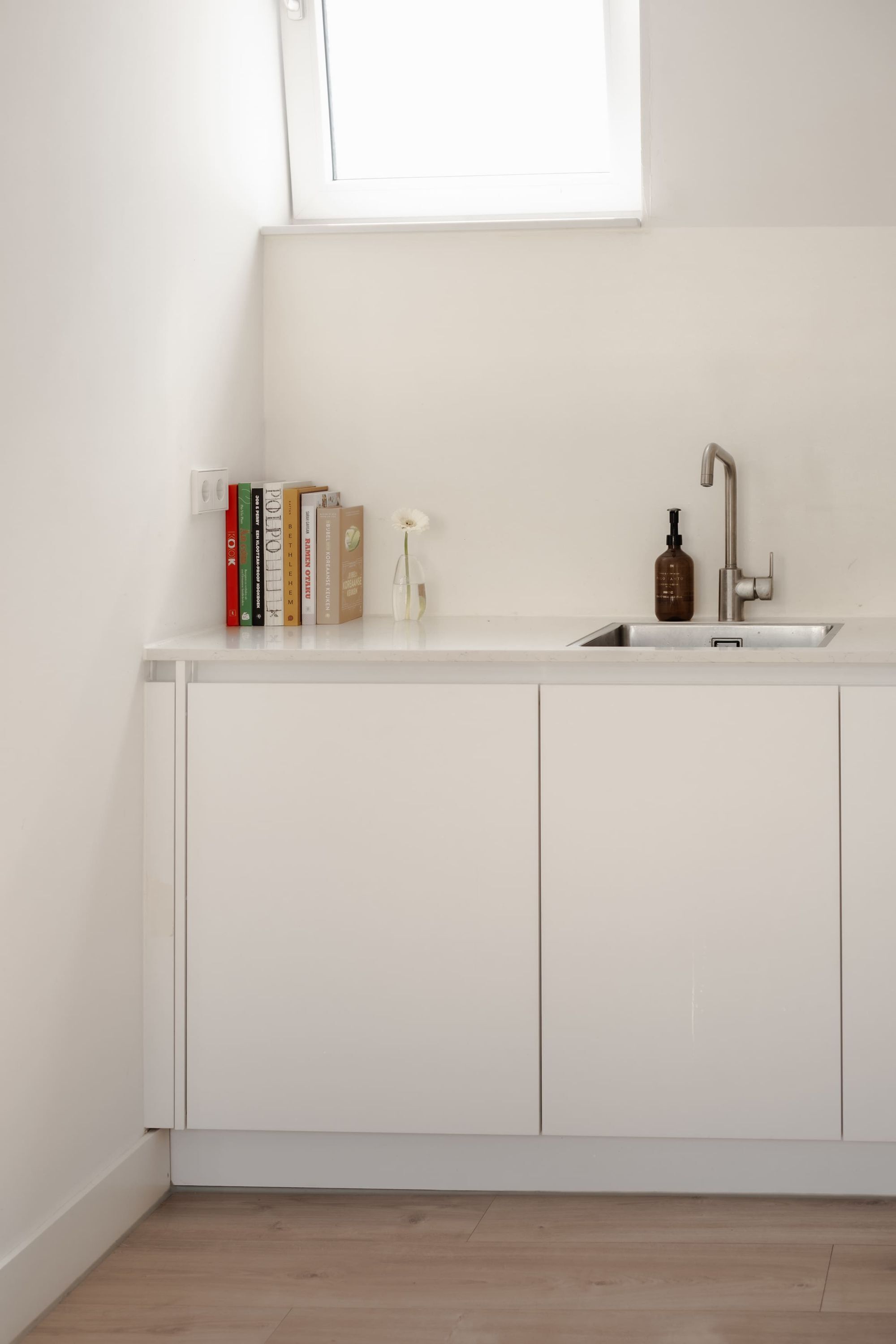 A minimalist kitchen with a white countertop, a built-in sink, and a window above the sink.