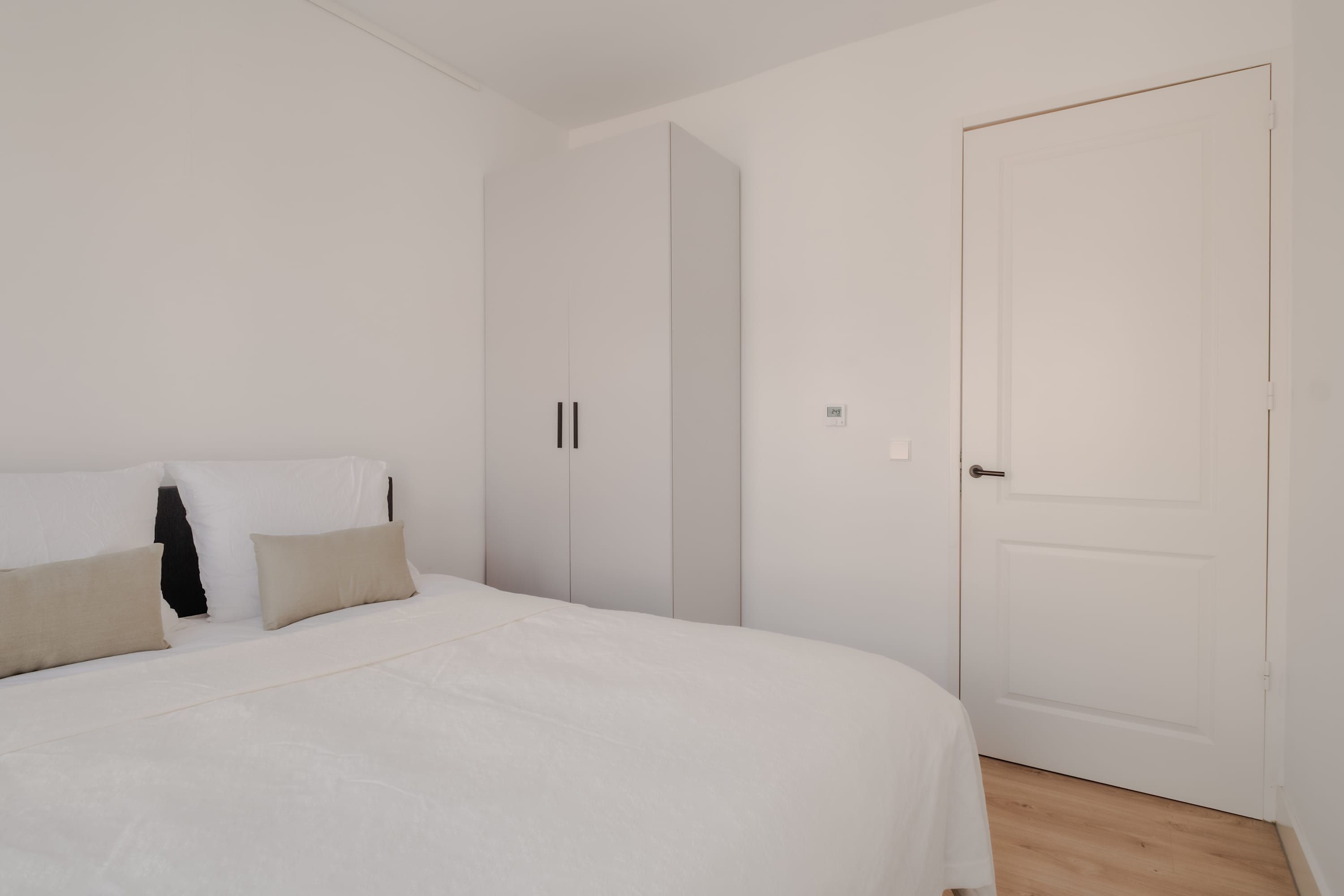A bedroom with a bed, pillows, a wardrobe, and a door.