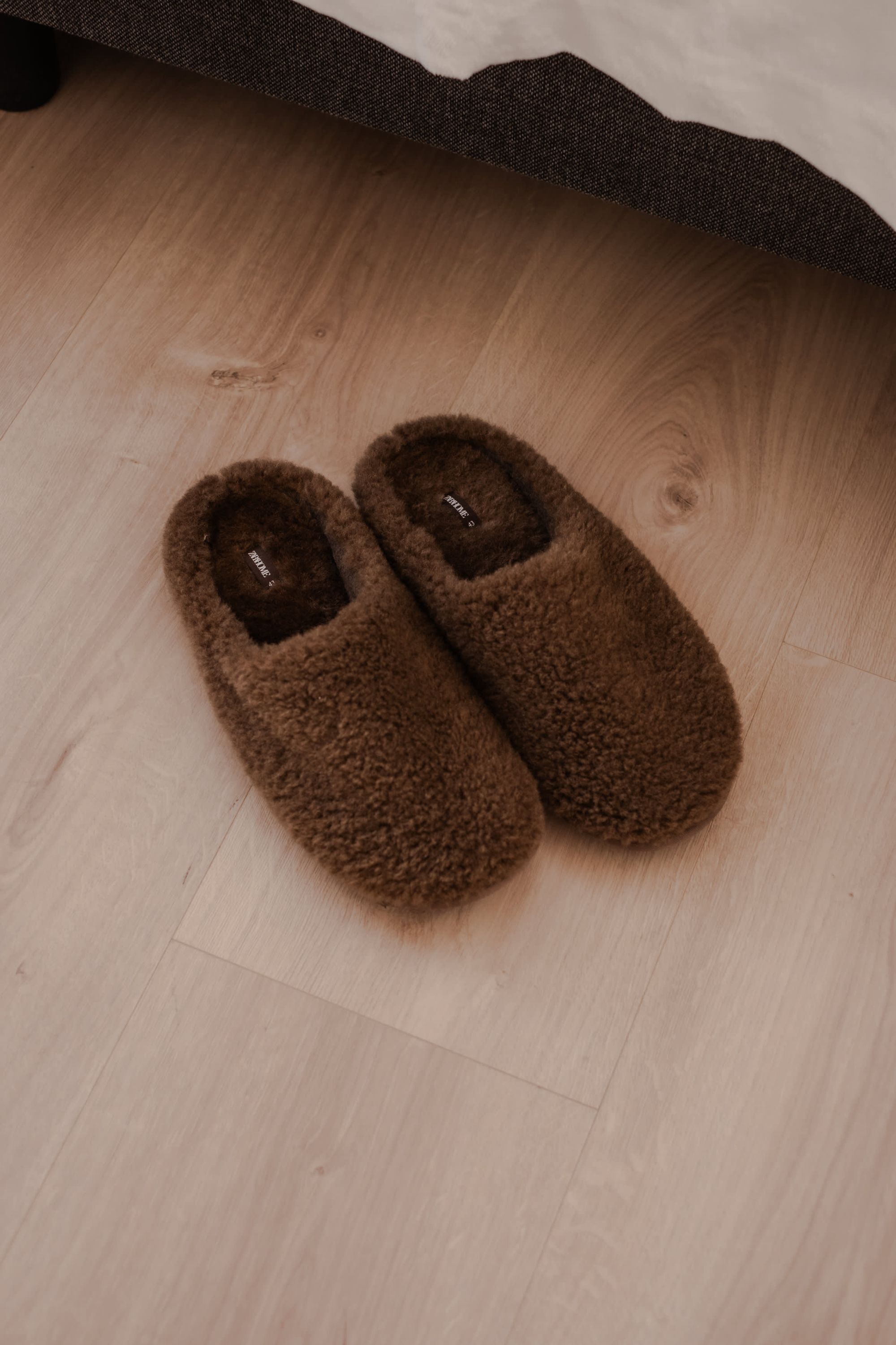 A pair of brown slippers on a wooden floor.