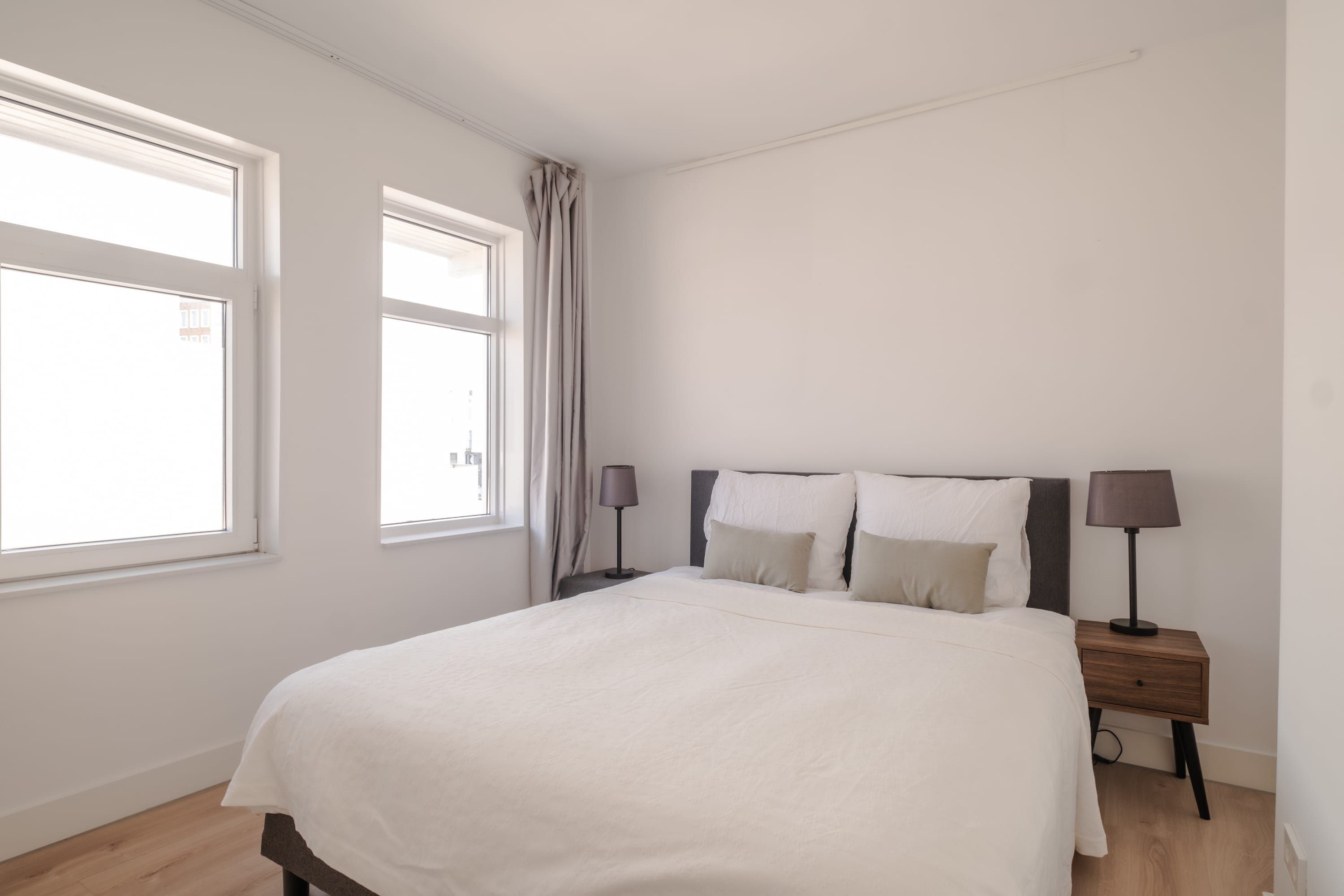 Une chambre à coucher avec un grand lit, deux tables de chevet et une fenêtre avec des rideaux.