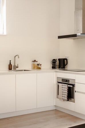 Una cucina moderna con mobili bianchi, lavello in acciaio inossidabile, macchina del caffè e forno.