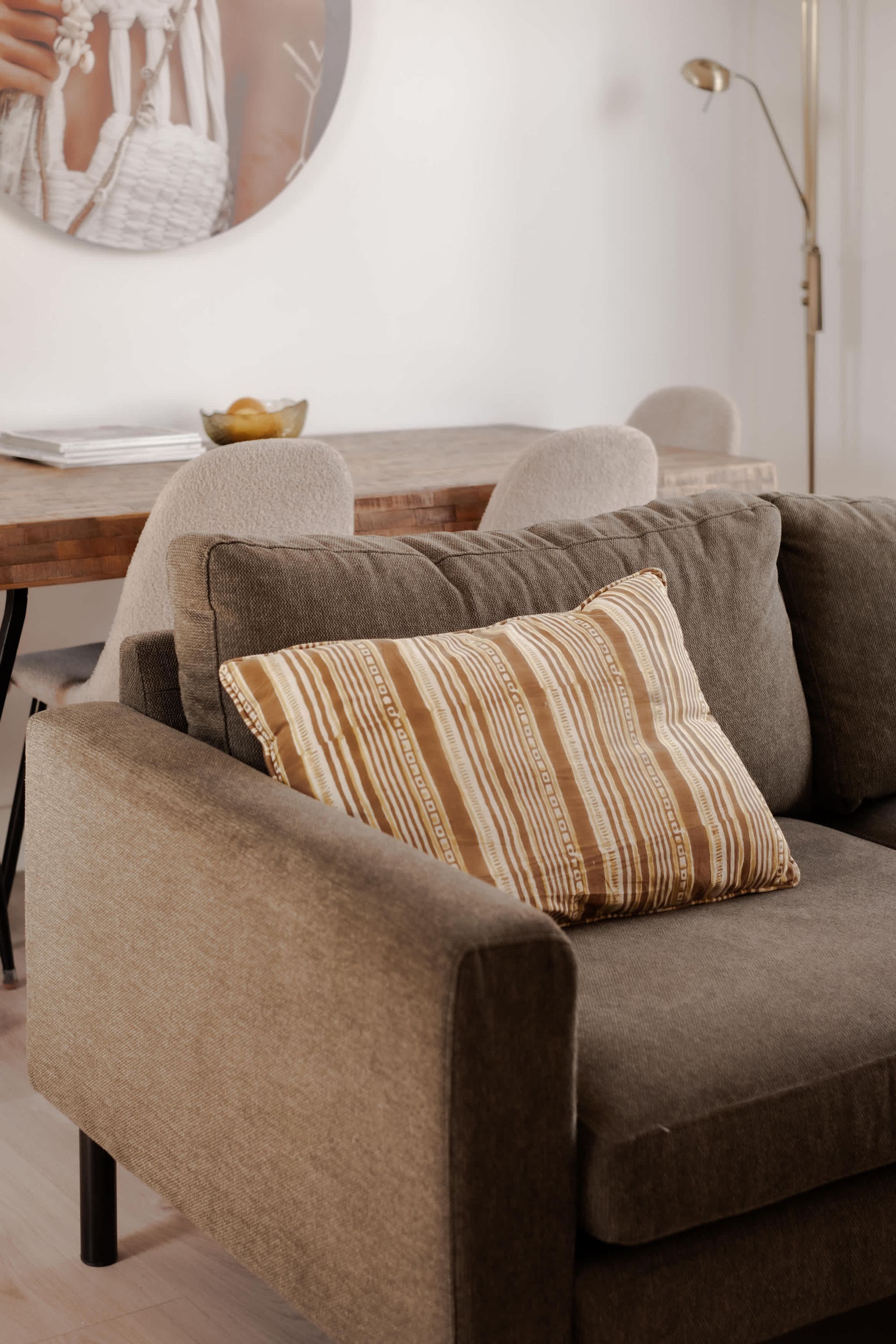 Un canapé avec un coussin à rayures, une table en bois avec un bol, et une lampe sur pied.