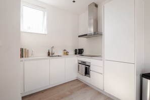 A modern kitchen with white cabinetry, a stainless steel range hood, a built-in oven, and a window above the sink. - In het Hart van Schiedam Rotterdam om de Hoek (Schiedam)