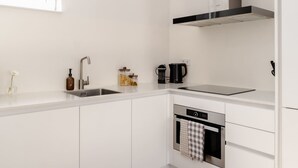 Uma cozinha moderna com armários brancos, coifa de aço inoxidável, máquina de lavar louça embutida e uma janela que proporciona iluminação natural.