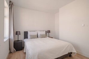 Ein Schlafzimmer mit einem Bett, Nachttischlampen, einem Nachttisch und einem Fenster mit Vorhängen.
