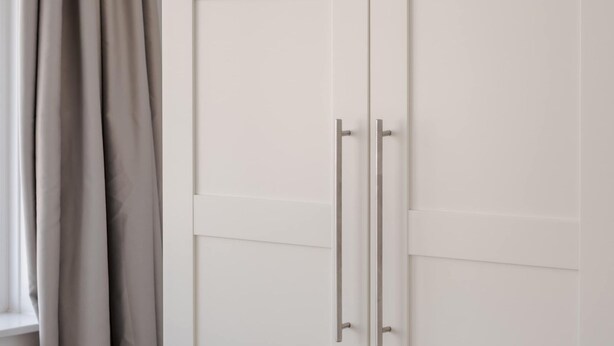 Um guarda-roupa branco com duas portas e puxador.