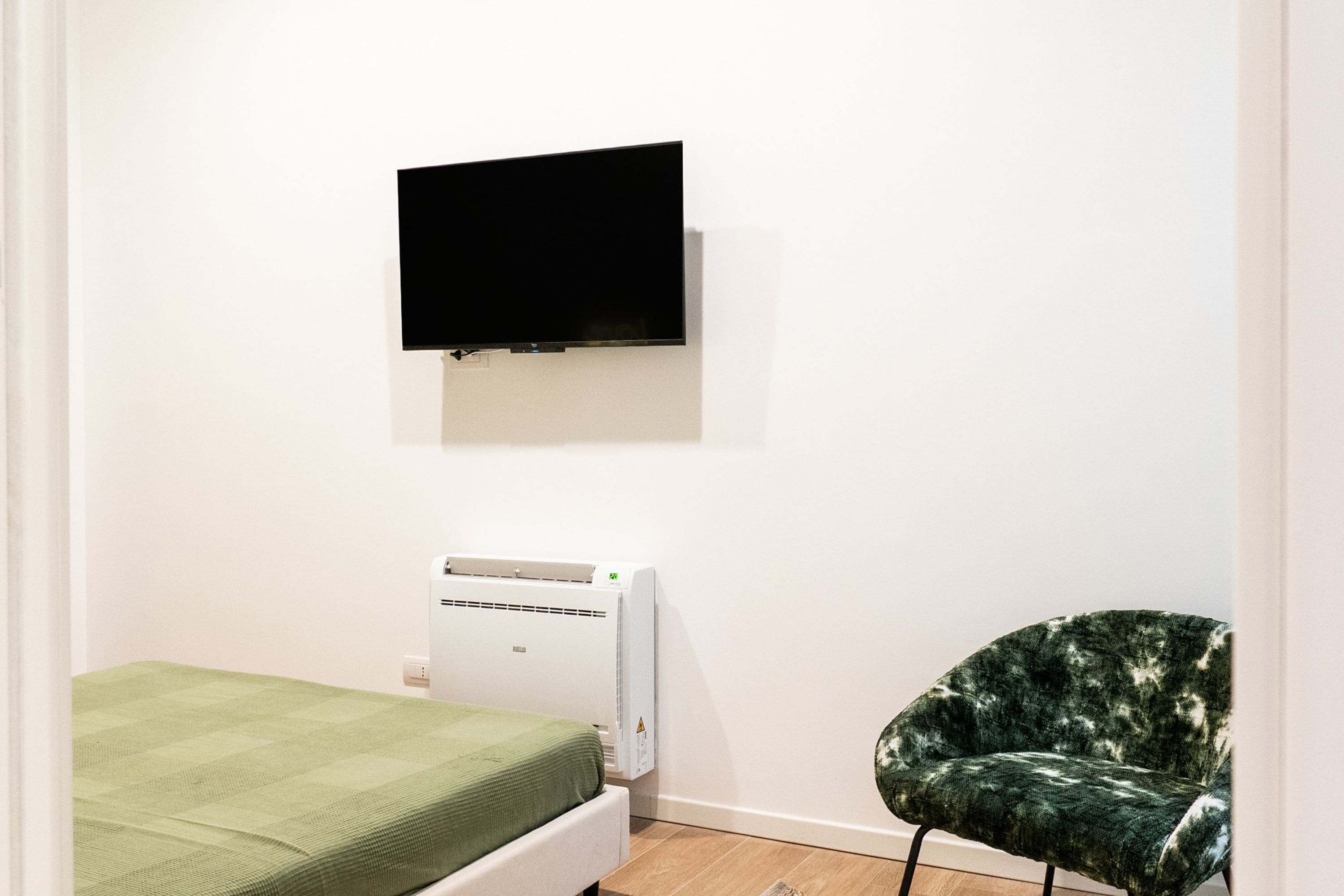 Una habitación con cama, televisor montado, aire acondicionado y una silla.