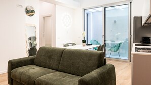 A modern living room with a green sofa, a dining area with a table and chairs, and a large sliding glass door leading to a balcony. - Cala Bianca Hideaway by Wonderful Italy (Polignano a Mare)