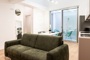A modern living room with a green sofa, a dining area with a table and chairs, and a large sliding glass door leading to a balcony. - Cala Bianca Hideaway by Wonderful Italy (Polignano a Mare)